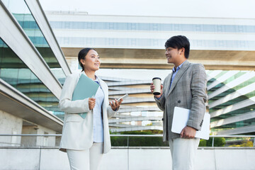 Two business professionals, Asian man in a suit and a woman in business attire, engaged in a...