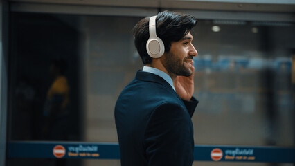 Closeup of smart executive manager listen relaxing music while waiting at train station. Happy male...