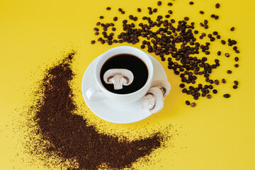 A white coffee cup and saucer stand on a yellow background. A slice of champignon mushroom floats in a cup, and coffee beans and ground coffee are scattered nearby. mushroom 