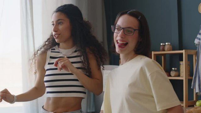 Medium shot of Caucasian teenage girl with cerebral palsy using walking stick while dancing at home with Biracial female best friend having fun together