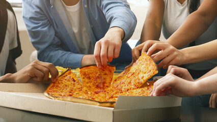 Cropped of group of friends are gathered around a table, eagerly reaching out to grab slices of a large pepperoni pizza from an open cardboard box during a casual social event