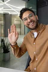 Smiling man waving during video call in modern office environment