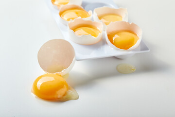 Rack for six broken eggs with whole yolks. One egg lies nearby, the yolk is on the table