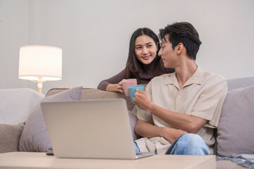 Fototapeta premium Young Asian couple in love Sitting and relaxing together in the living room happily. Couple making romantic love in the living room