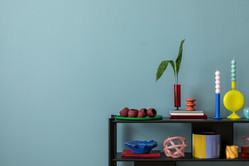 Colorful composition on blue wall with black shelf, design accessories, and decorations vases with leaf, candels and copy space. Home decor. Template...