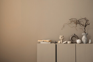 Minimalist composition of warm and cozy living room interior with copy space, brown sideboard, gray vase with branch, books, casket, stylish sculpture and personal accessories. Home decor. Template.