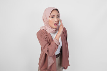 Young Asian Muslim woman wearing hijab hand on mouth whispering or telling secret conversation.