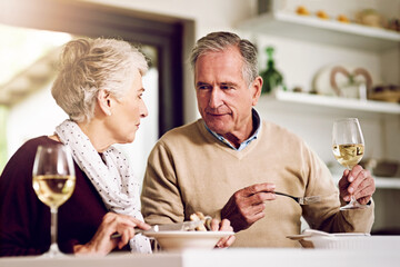 Senior couple, dinner and talking in home for anniversary, date or retirement with love in marriage. Elderly, people and eating together with wine drink and happy for romance, relationship or bonding
