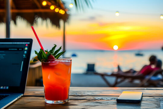 The image captures a refreshing cocktail and a laptop on a table against the backdrop of a serene beach sunset, symbolizing remote work-life balance