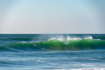 Une belle vague couleur émeraude se forme dans les eaux turquoises de la mer d'Iroise, laissant derrière elle écume et embruns.