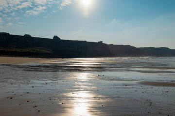 Le reflet étincelant du soleil danse sur le sable mouillé de la plage de Pen Hat, tandis qu'en arrière-plan, les falaises imposantes ajoutent une touche de grandeur à ce paysage côtier enchanteur.