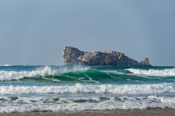 Devant le rocher du Lion, les vagues se brisent avec puissance, projetant des embruns dans l'air et laissant derrière elles une écume blanche éclatante.