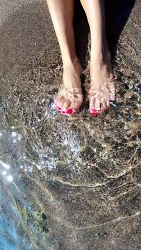 Women's feet in the sea waves on the beach. Top view of body part. Pedicure foot fingers.