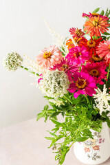 Summer bouquet of colorful Zinnia, onion inflorescences and mint sprigs, bouquet of flowers on the table near the wall, home decoration with flowers
