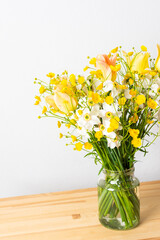 Spring bouquet of yellow buttercups, white daffodils and tulips, bouquet of flowers on the table near the wall, home decoration with flowers