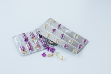 On a light background lie two blisters with capsules and lilac flowers inside. nearby are several...