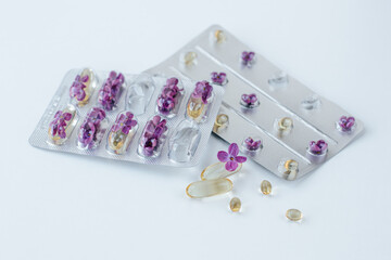 On a light background lie two blisters with capsules and lilac flowers inside. nearby are several capsules of different sizes and shapes and a lilac flower. Allergy medications