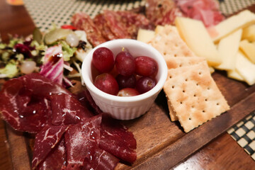 close up of cheese, ham, grape, raisin, biscuit, olive and salad platter on a wooden plate