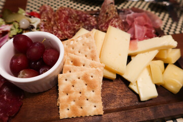 close up of cheese, ham, grape, raisin, biscuit, olive and salad platter on a wooden plate