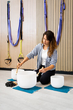 Vertical photo of an adult woman performing a sound bath session with quartz bowls inside a room.Concept of sound therapy. Vibrational Therapy that uses the effect of sound.