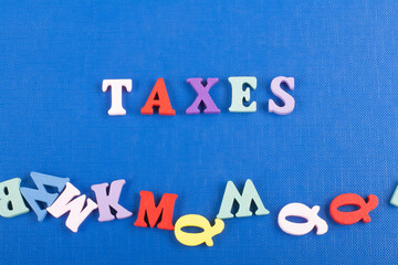 TAXES word on blue background composed from colorful abc alphabet block wooden letters, copy space...