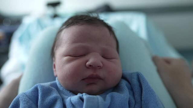 Newborn baby sleeping on a soft surface, dressed in a cozy blue onesie. peaceful and serene expression of the baby highlights the comfort and tranquility of a newborn&rsquo;s sleep in early infancy