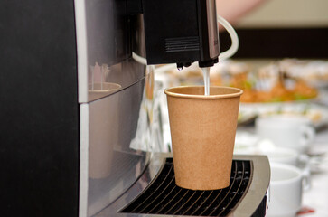 Coffee machine makes coffee with milk in a paper brown cup at a public event, banquet, without...