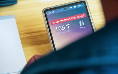 Excessive heat warning of 105 degree Fahrenheit with haze weather alert on smartphone screen. Close...