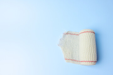 A white bandage with red stripes is laying on a blue background. The bandage is torn and frayed,...