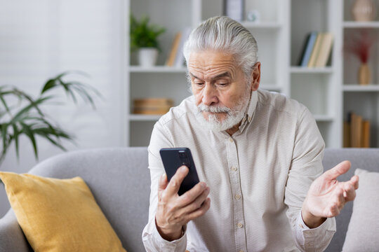 Senior man using smartphone on sofa looking confused and frustrated at home