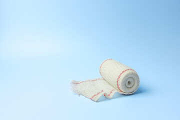 A white bandage is laying on a blue background. The bandage is rolled up and has red and white...