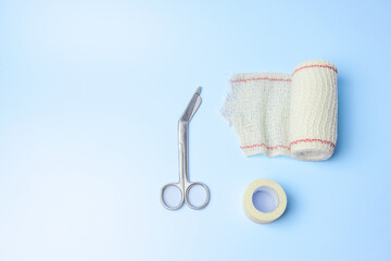 A pair of scissors and a roll of gauze are on a blue background. The scissors and gauze are...