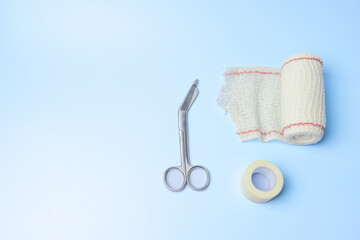A pair of scissors and a roll of gauze are on a blue background. The scissors are silver and the...