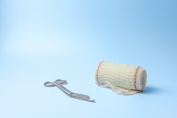 A pair of scissors and a roll of gauze are on a blue background. The scissors and gauze are placed...