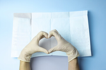 A person wearing gloves is making a heart shape with their hands on a piece of paper. Concept of...