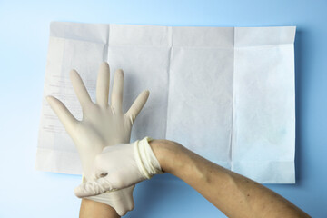 A person wearing a pair of latex gloves is holding a piece of paper. The gloves are white and the...