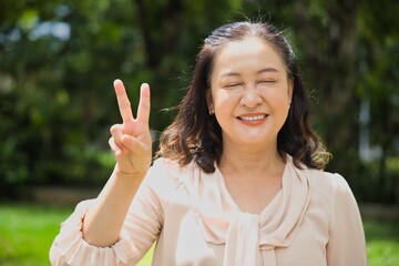 Happy blind middle aged asian woman pointing 2 fingers up, concept of v for victory, concept image...