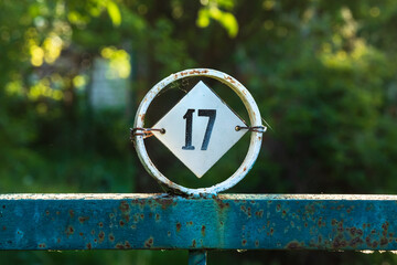 Number 17 iron plate on a fence or gate. Number seventeen, metal rhombus in a circle on the street