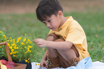 Happy little 4 year old Caucasian boy looking and touching flowers, smiling, sunny day. Cute child...