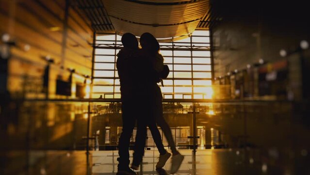 Silhouette of man and a woman meeting in airport terminal or train station after arrival. People hugging. Concept of travel, tourism and transport. Long-awaited meeting. Sunset panoramic window.