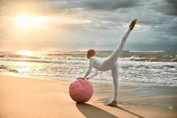 Hairless ballerina with alopecia in white futuristic suit dancing with pink sphere at sunset sea,...