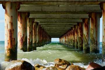 Rusty pillars of old sea pier create mesmerizing seascape scene with view from under pier, restless...