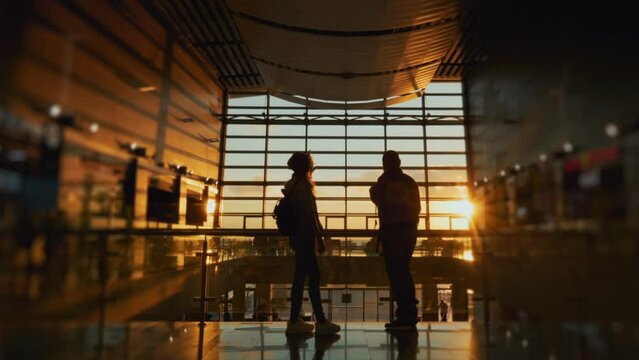 Silhouette of man and a woman meeting in airport terminal or train station after arrival. People talking. Concept of travel, tourism and transport. Long-awaited meeting. Sunset panoramic window.