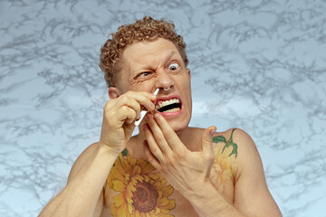 Funny image of shirtless emotional man taking care after his look, using tweezers for nose hair...