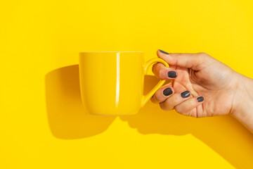 Hand holding yellow ceramic mug on yellow background