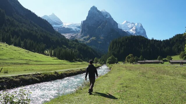 Scenic view of Rosenlaui with Wellhorn mountain and male tourist walking along Reichenbach river on sunny day at canton of Bern, Switzerland