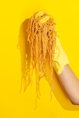 Hand holding cooked spagetti pasta on yellow background