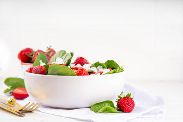 Spinach and strawberry summer salad with cottage cheese and balsamic sauce, fresh raw ripe fruit vegetable salad bowl, healthy diet food, on white kitchen table with cutlery