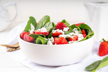 Spinach and strawberry summer salad with cottage cheese and balsamic sauce, fresh raw ripe fruit vegetable salad bowl, healthy diet food, on white kitchen table with cutlery