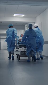 Doctors, nurses and paramedics run and push stretcher with seriously injured patient to surgery room. Medical personnel save human life in emergency department. Medical facility hallway.Vertical shot